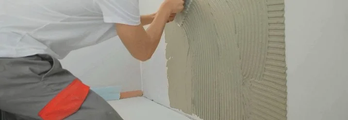 Person trägt Fliesenkleber mit Kelle auf